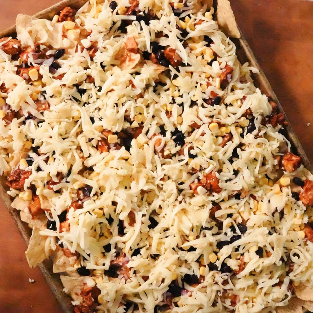 cheese layered over loaded nachos on a baking sheet.