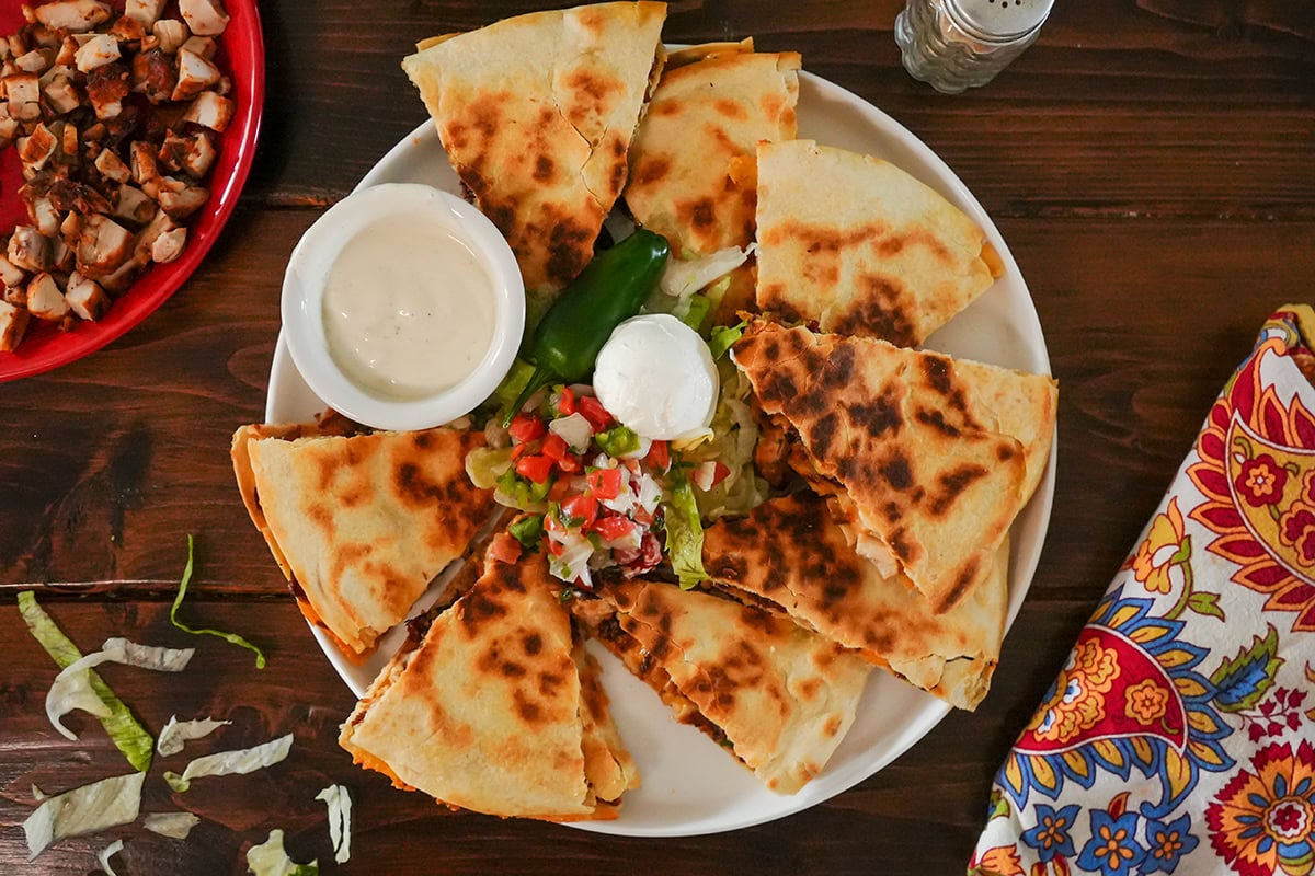 a quesadilla cut into pieces served with sour cream and pico salsa.