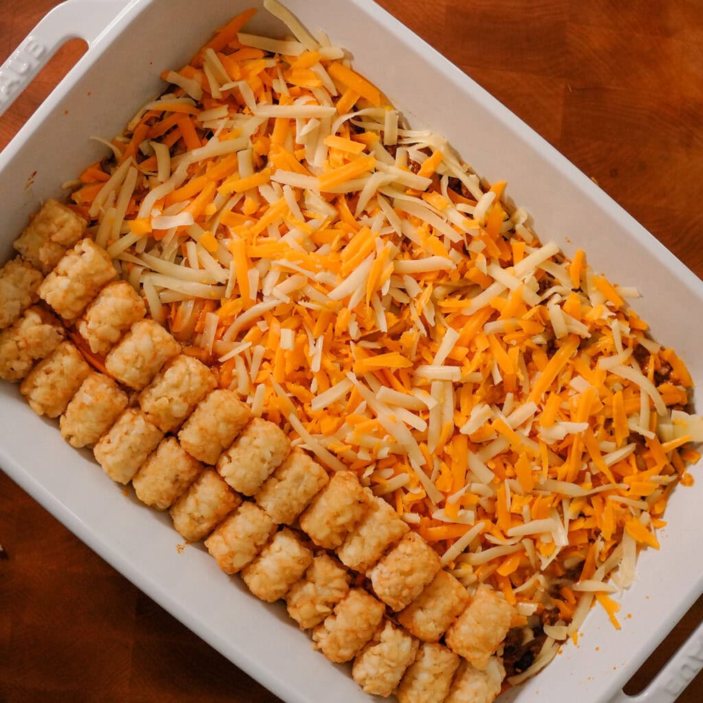tater tots layered over cheese in a baking dish.