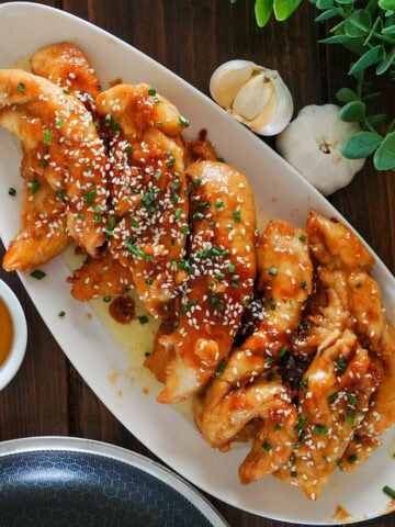 honey garlic chicken fingers on a plate with dipping sauce.