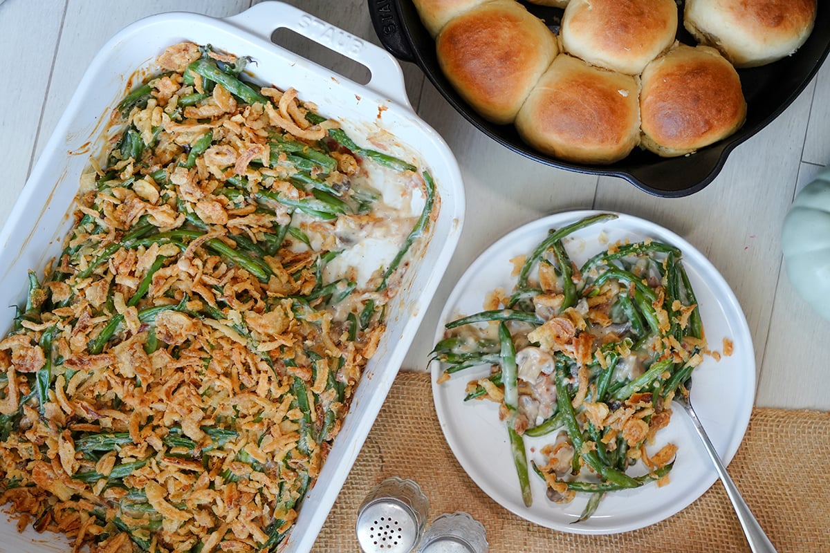 a bacon and green bean casserole with french's onions next to a skillet of dinner rolls.