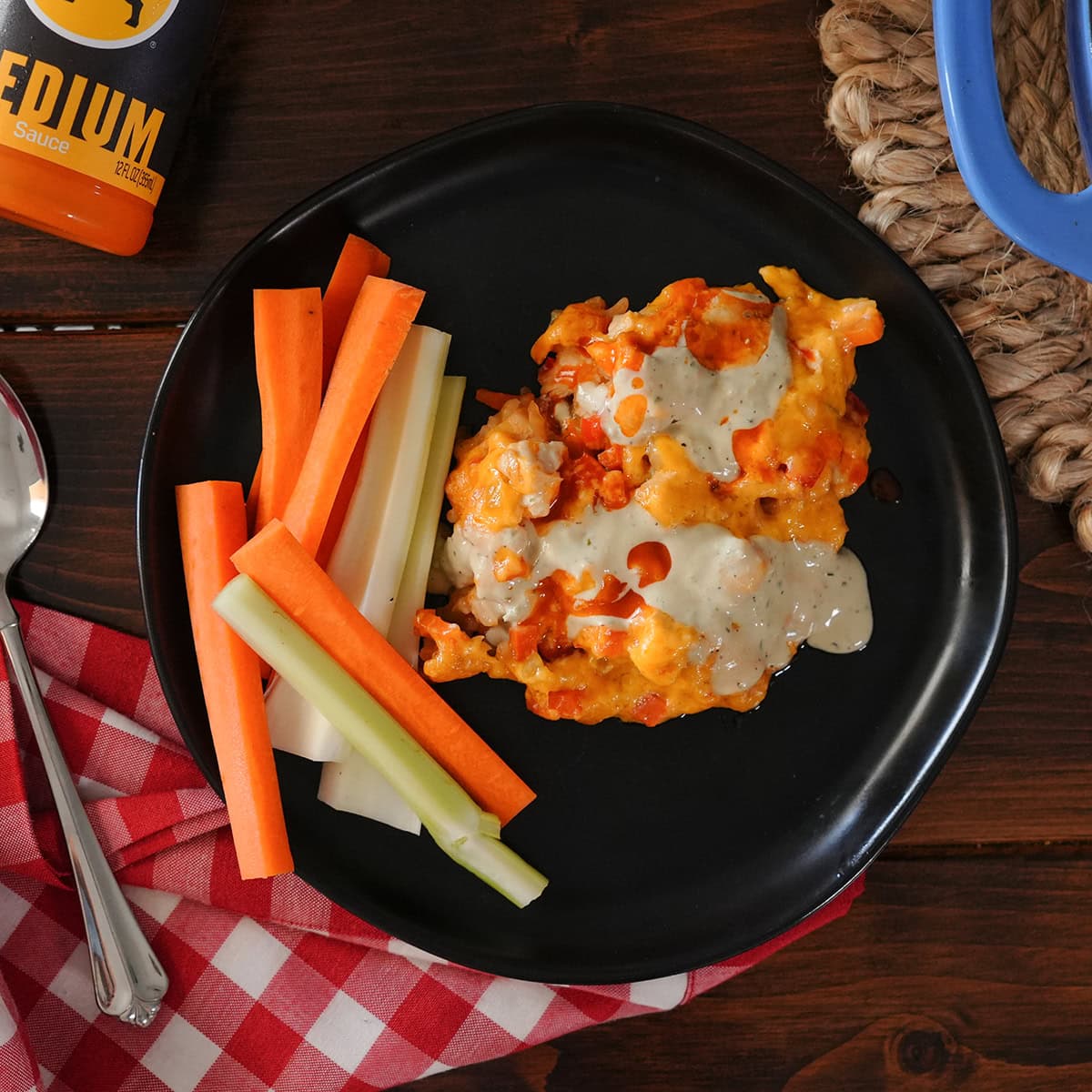 Buffalo chicken casserole on a plate with ranch dressing and hot sauce.