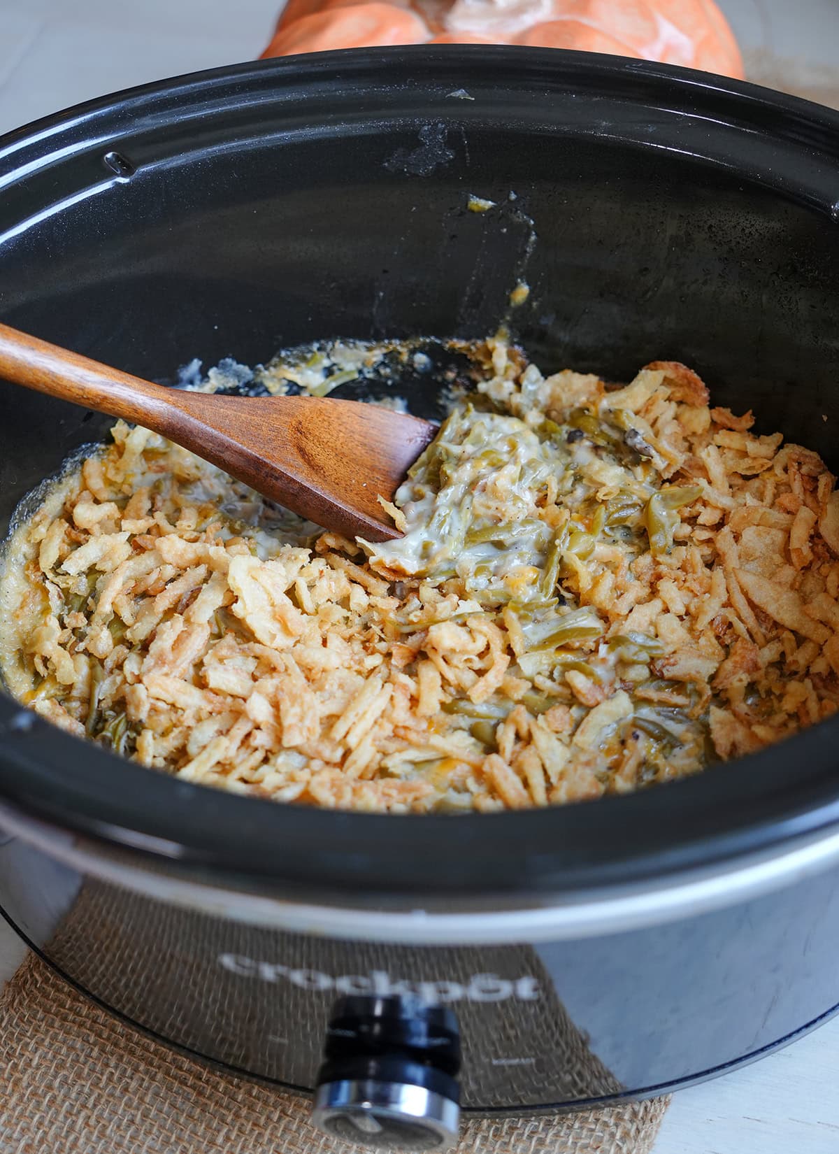 slow cooker green bean casserole with a wooden spoon and french's onion topping.