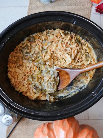 crockpot green bean casserole with a wooden spoon and crispy onion topping.