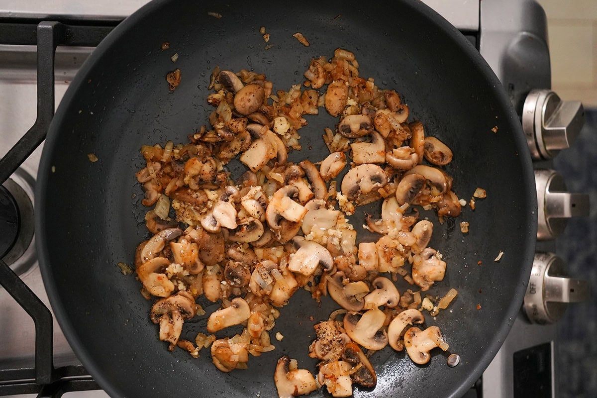 mushrooms and onions sautéing in a skillet.
