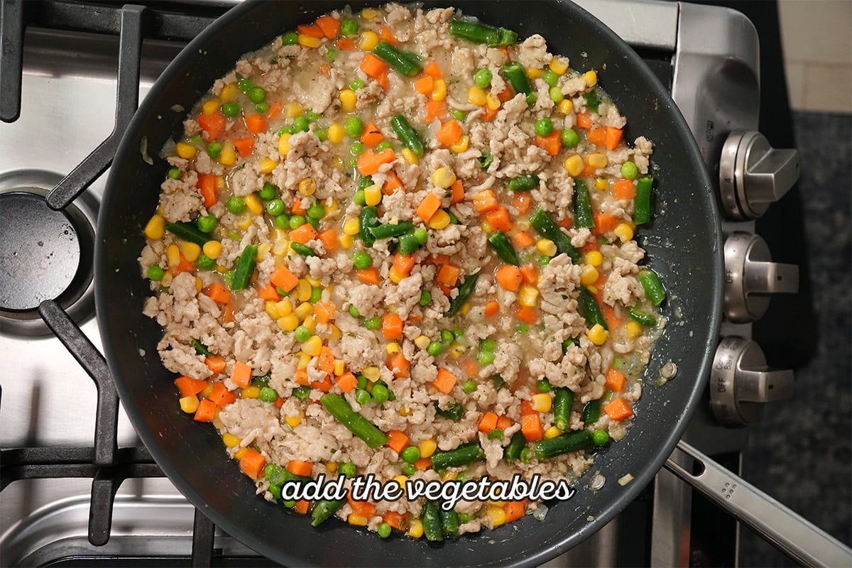 vegetables and broth added to a chicken mixture in skillet.