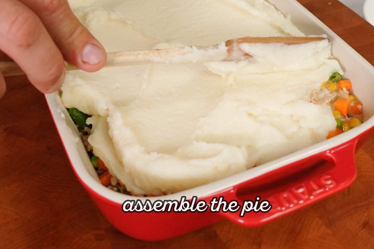 mashed potatoes spreading over chicken mixture in a baking dish.