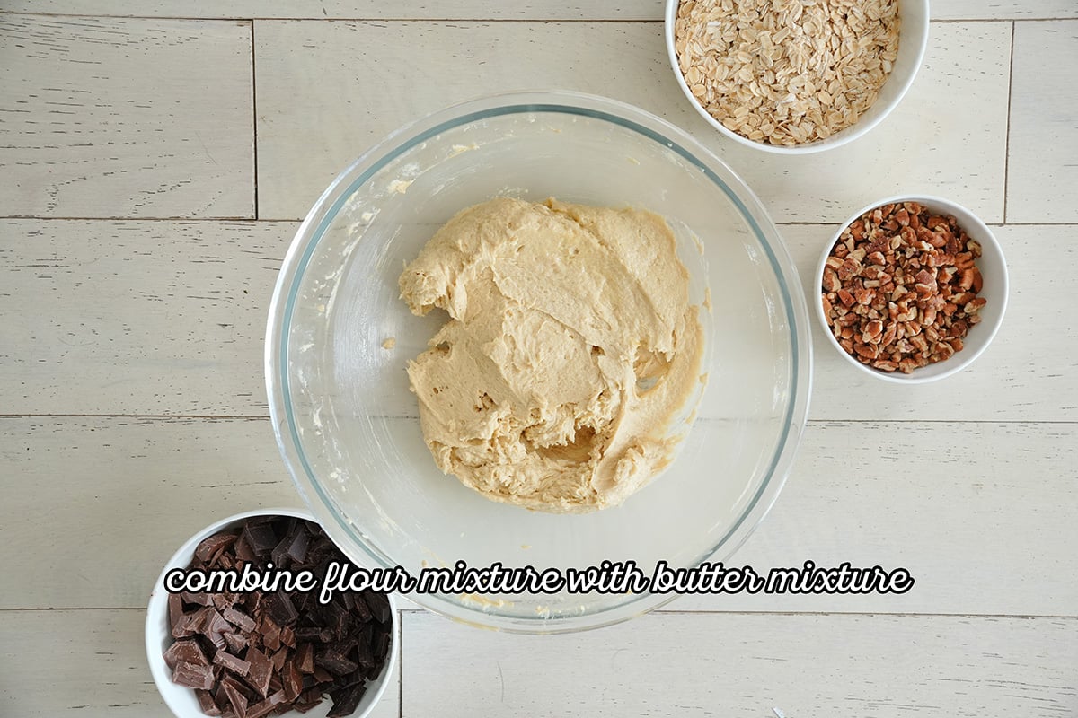 cookie dough in a bowl next to chocolates, pecans and oats.