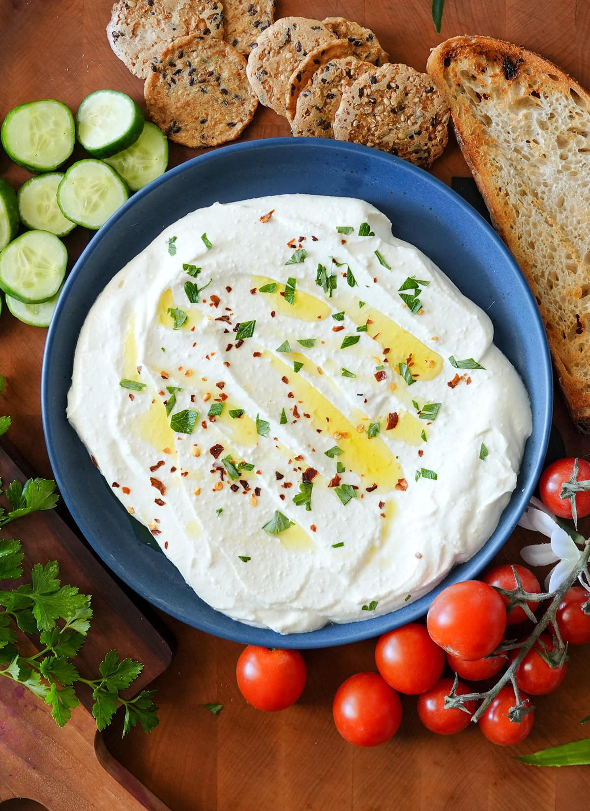 A whipped feta cheese dip spread over a plate topped with herbs.